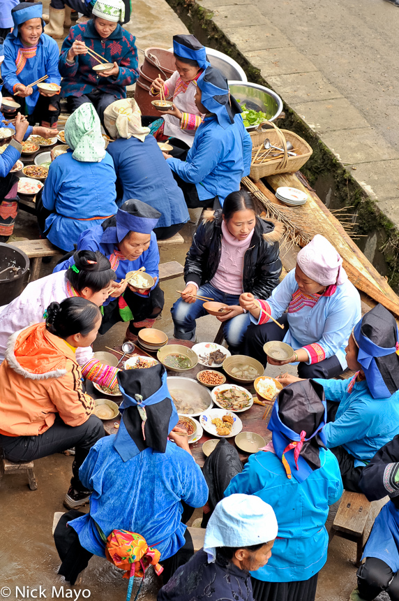 A group of Miao women in traditional clothes and hats eating a celebratory lunch in Xing Hwa.