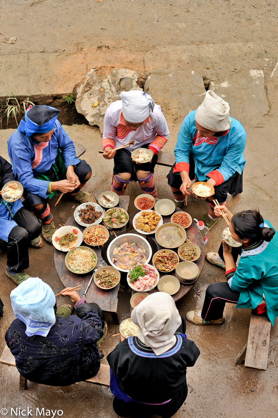 A group of Shui women, with one Miao dressed in blue clothes and hat, eating a celebratory lunch in Xing Hwa.