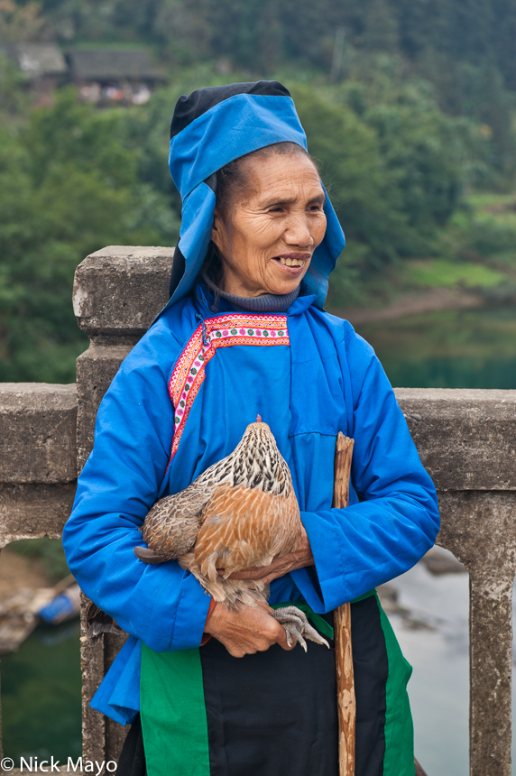 A Miao woman, dressed traditionally in blue clothes and hat, holding a chicken purchased at Bakai market.