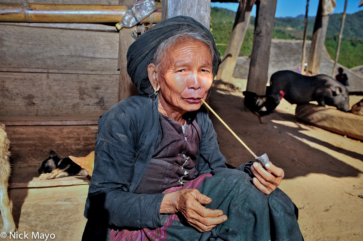 An older Bulang lady smoking a long stemmed pipe in the shade in Xinnan village.