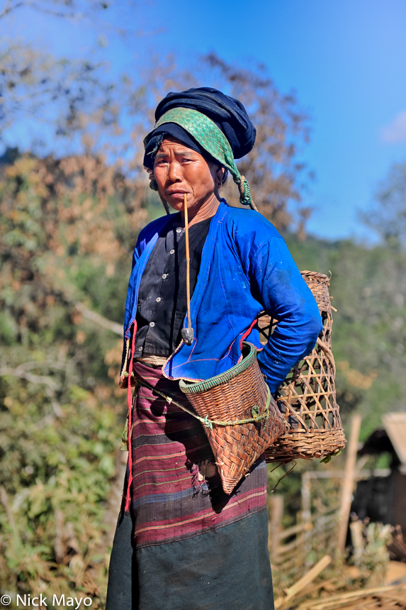 A woman from the Bulang village of Xinnan smoking a long stemmed pipe while heading to the fields.