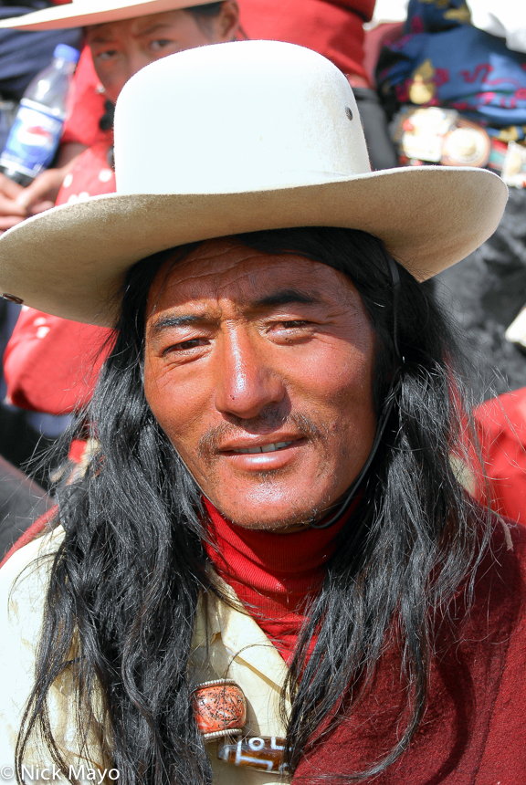 A Khampa Tibetan man wearing a cowboy hat over long hair at a Sershul horse festival.