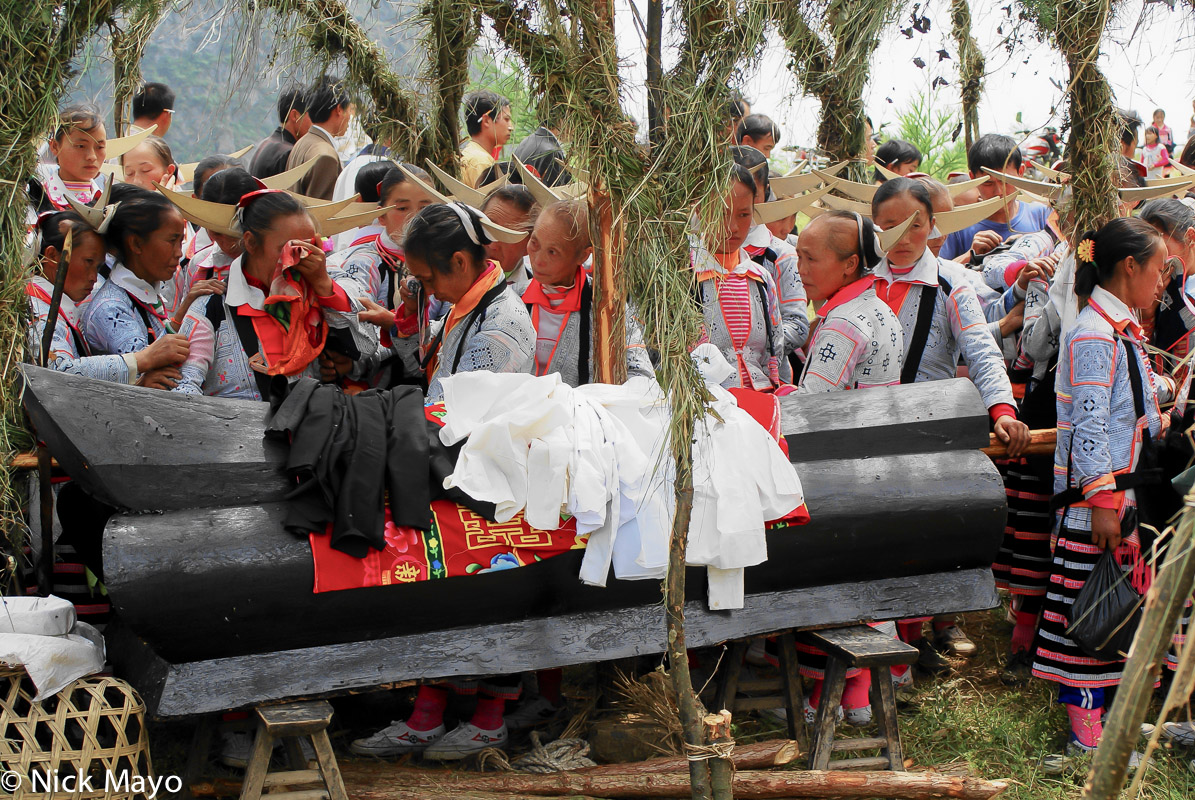 Qing Miao women wearing traditional wooden hair pieces mourning around the coffin at a funeral in Longee.