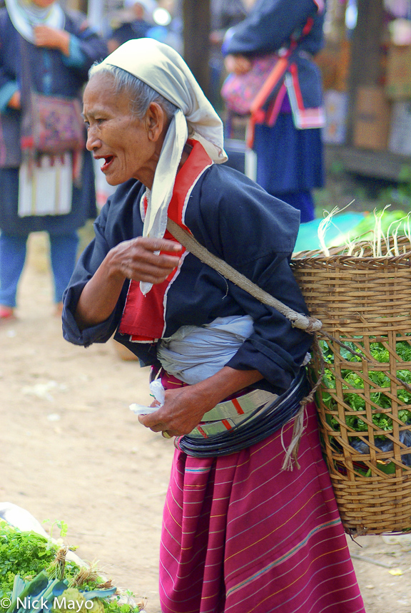 A Palaung woman carrying a basket and wearing traditional waist hoops shopping at Katai market.