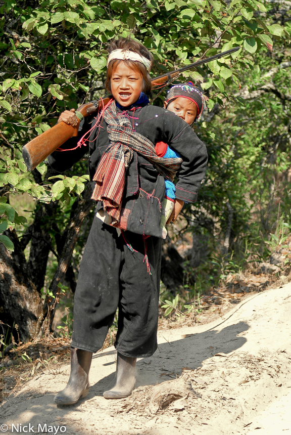 A young Eng man carrying a gun and baby while on a hunting trip near Ban Lu village.