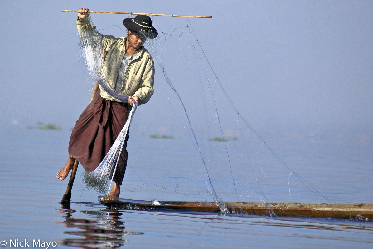 An Intha leg rower fishing with a net from his boat on Inle Lake.