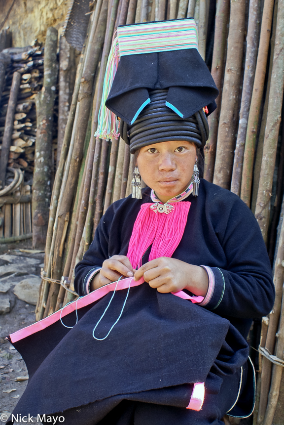 A Pintoh Yao girl wearing a traditional flat topped hat stitching in Nan Ke village.