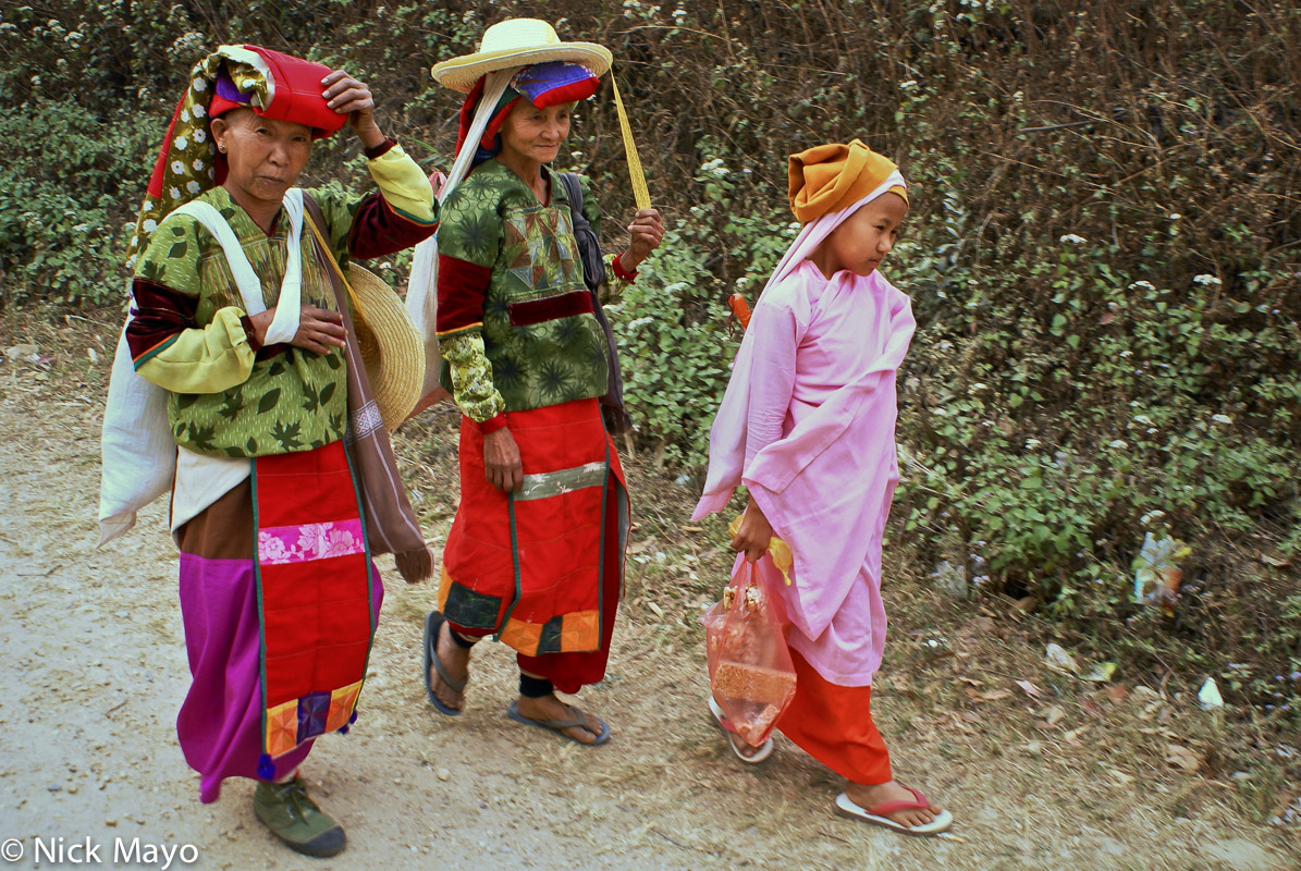 Two older Golden Palaung women in festival attire and traditional turbans returning home to Namshan accompanied by a young nun...