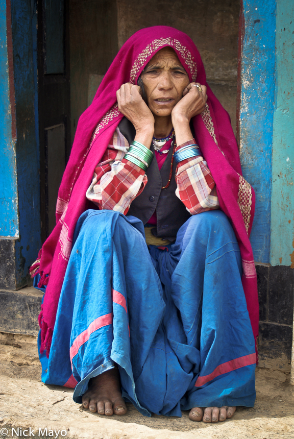 A lady in a magenta head scarf resting in the doorway of her Ram Ganga valley home.