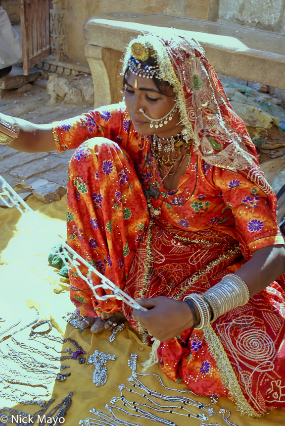 An elegantly dressed jewellry seller at Jaisalmer Fort wearing a gold fringed head scarf, necklace, bracelets and nose stud.