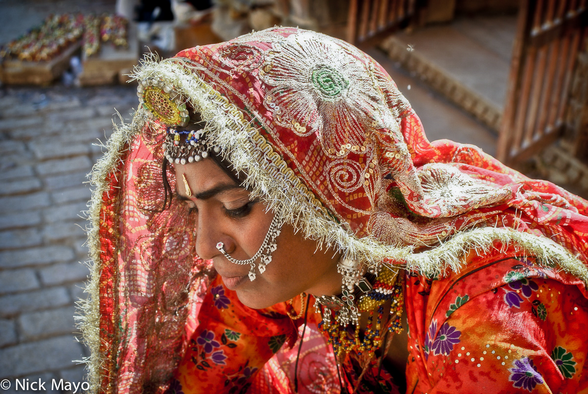 An elegantly dressed jewellry seller at Jaisalmer Fort wearing a gold fringed head scarf, necklace and nose stud.