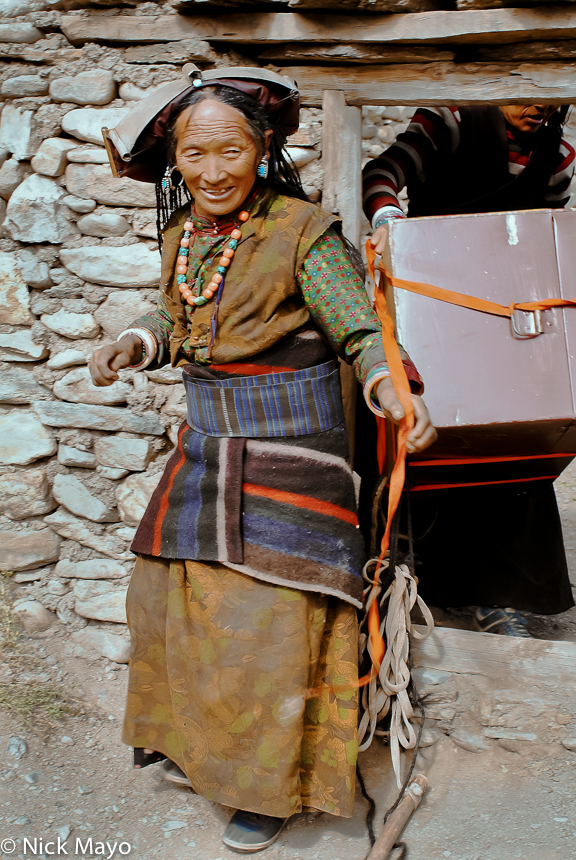 A Dolpo-pa woman of Dol wearing a traditional brass hat unloading goods brought back from Tibet.