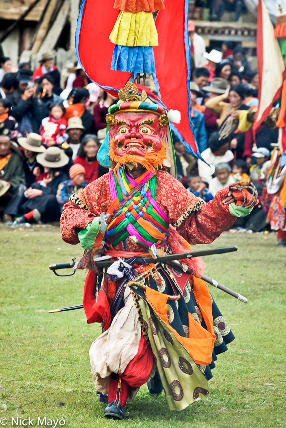 A red masked Tibetan monk carrying a sword dancing at a festival at the Yazer Gon monastery in Manigango.