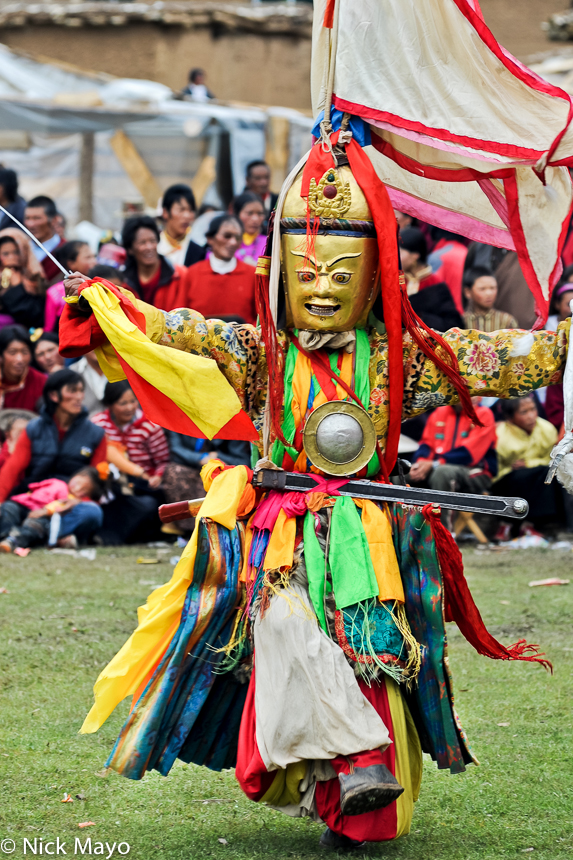 A gold masked Tibetan monk carrying a sword dancing at a festival at the Yazer Gon monastery in Manigango.