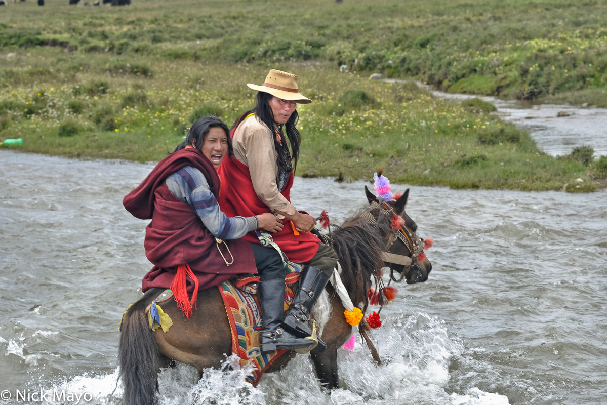 A Khampa Tibetan man crossing a river by horse with his partner during a festival at Sershul.