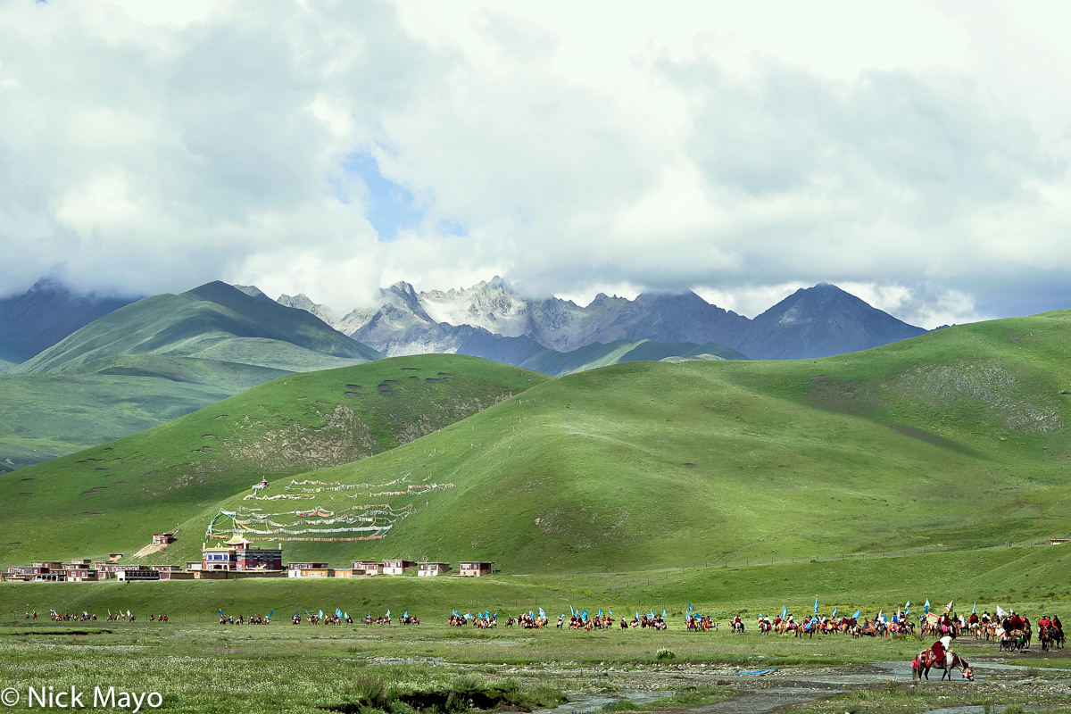 A long line of standard bearing Tibetan horsemen passing in front of a monastery en route to a grassland festival near Manigango...