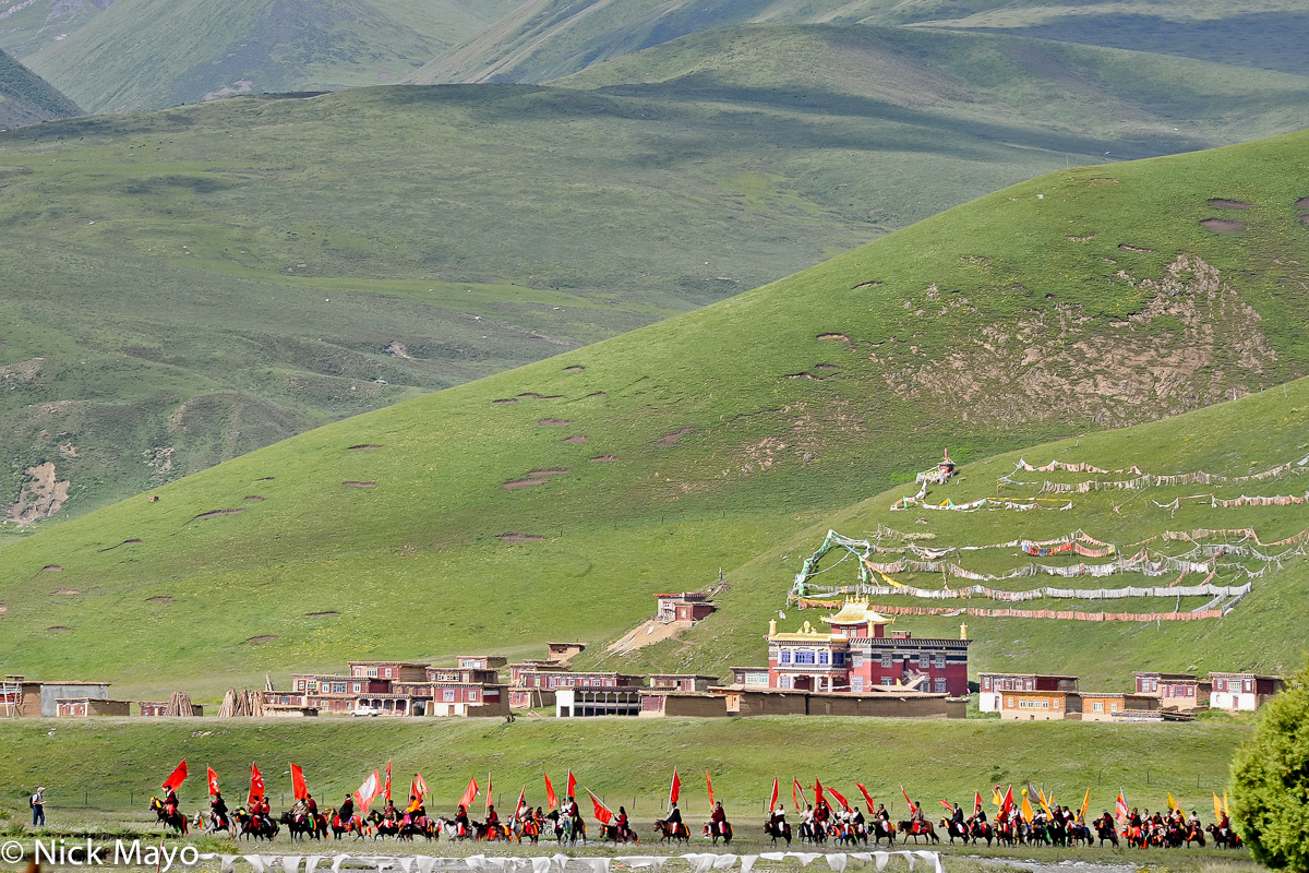 A line of standard bearing Tibetan horsemen passing a monastery en route to a grassland festival near Manigango.