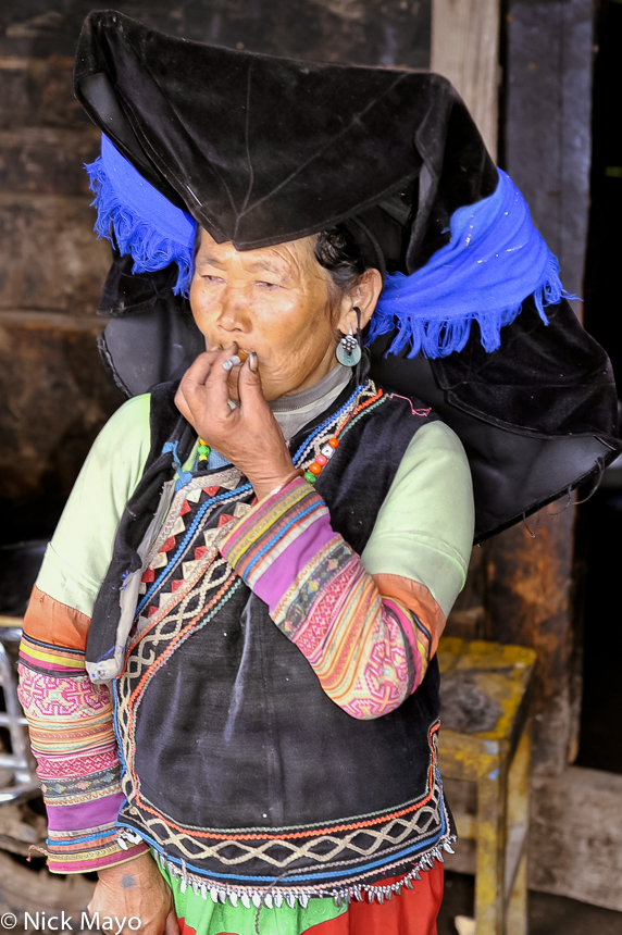 A traditionally dressed Yi woman wearing a mortar board style hat smoking at Da Ya Chang.