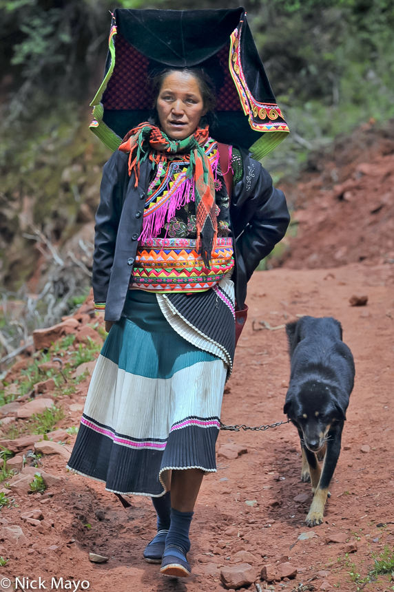 A Yi woman wearing a mortar board style hat with her dog at Da Ya Chang.