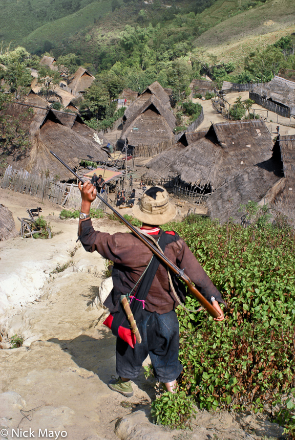 An Eng man on a hunting trip carrying his gun into the thatch village of Ban Nong.