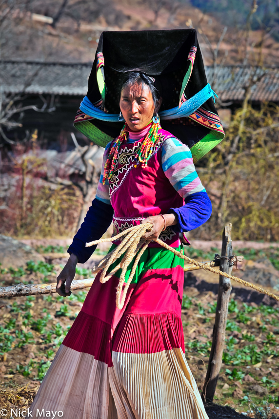 A traditionally dressed Yi woman, wearing a mortar board style hat and hanging beaded earrings, at Hoshi.