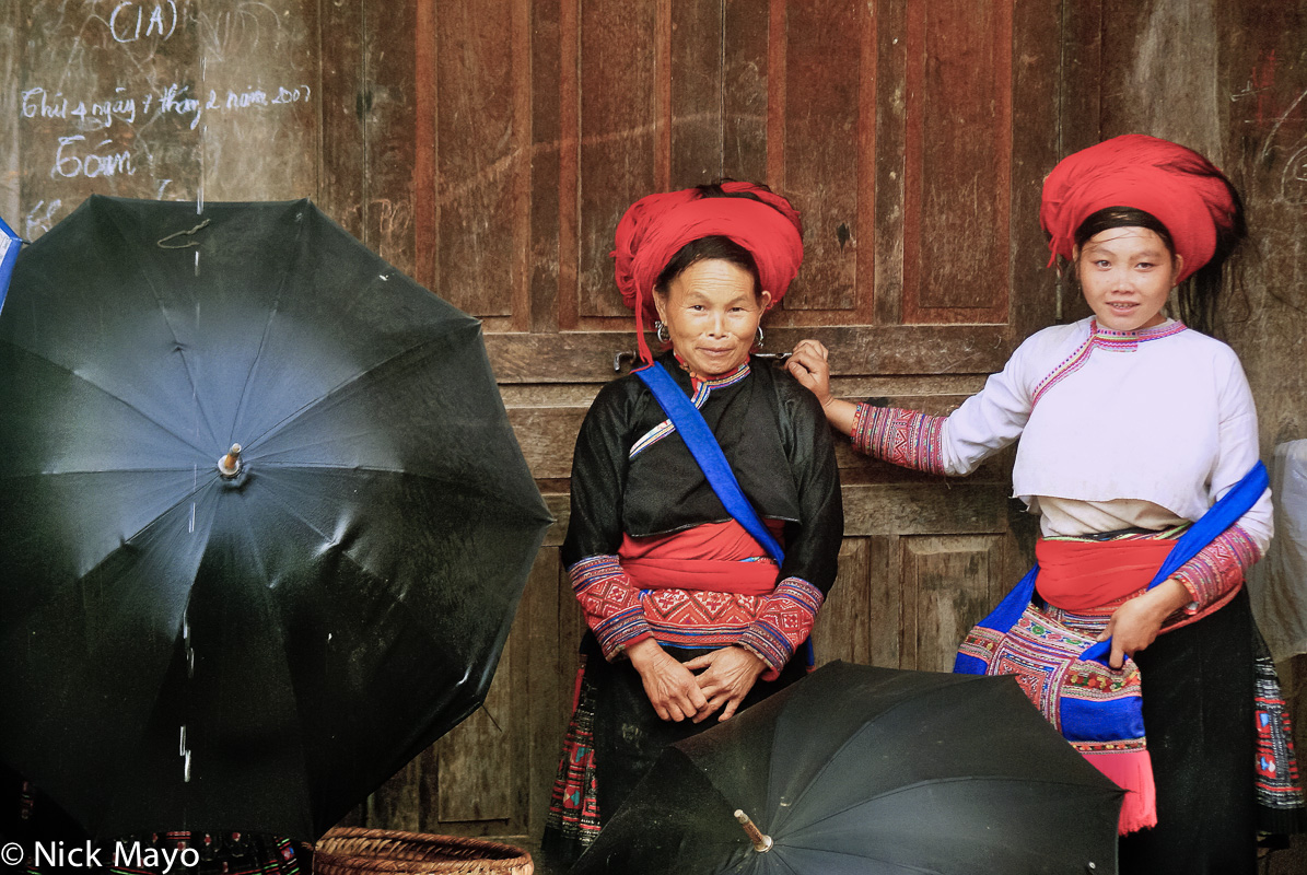 Two Red Hmong women sheltering behind umbrellas during a shopping rain break at Sin Ho market.