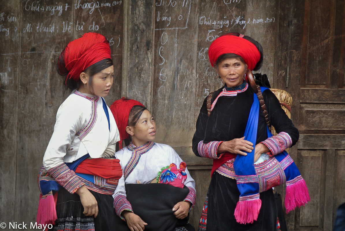 Three Red Hmong women wearing traditional hair pieces taking a shopping break at Sin Ho market.