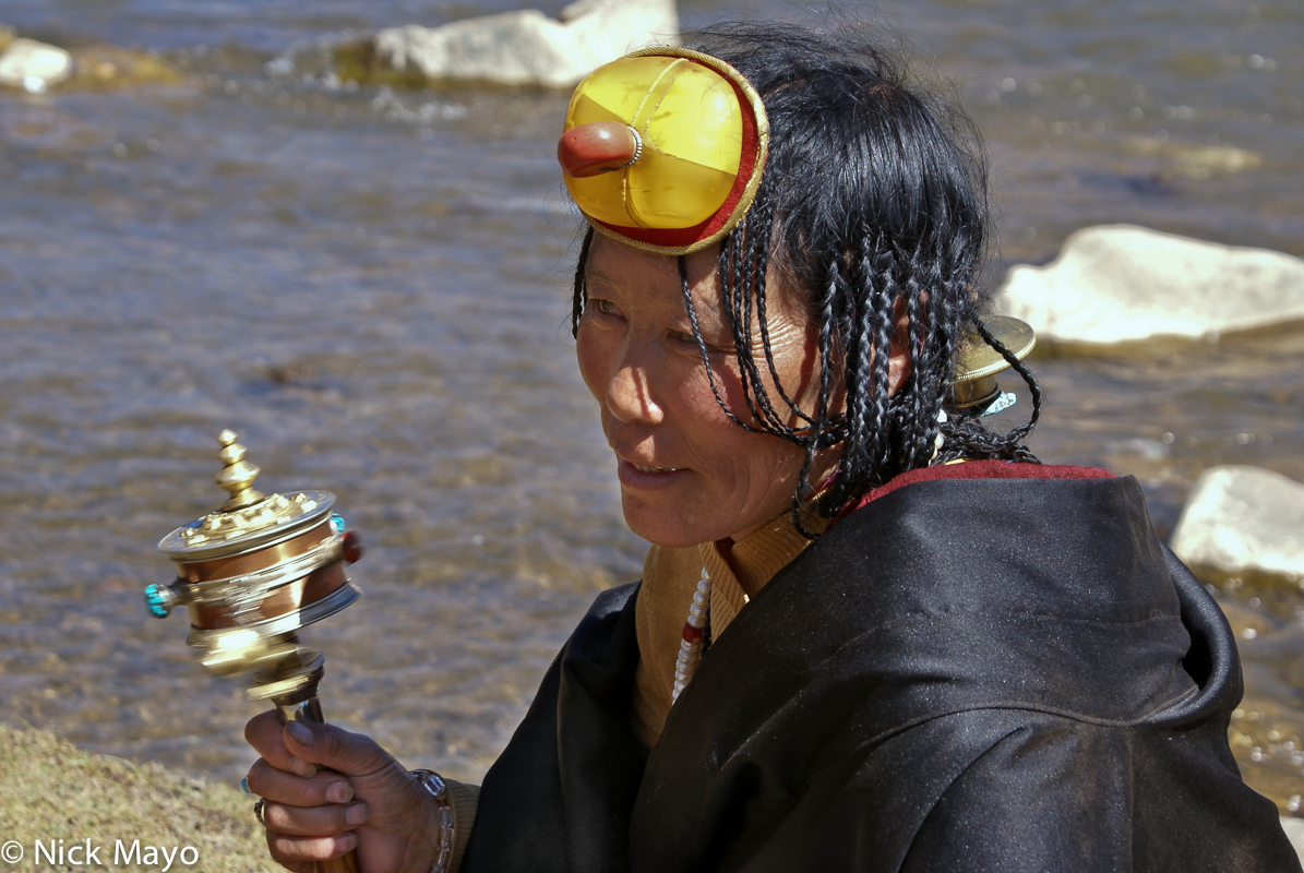 A Tibetan woman wearing an amber hair piece and carrying a prayer wheel attending an assembly at Sershul monastery.