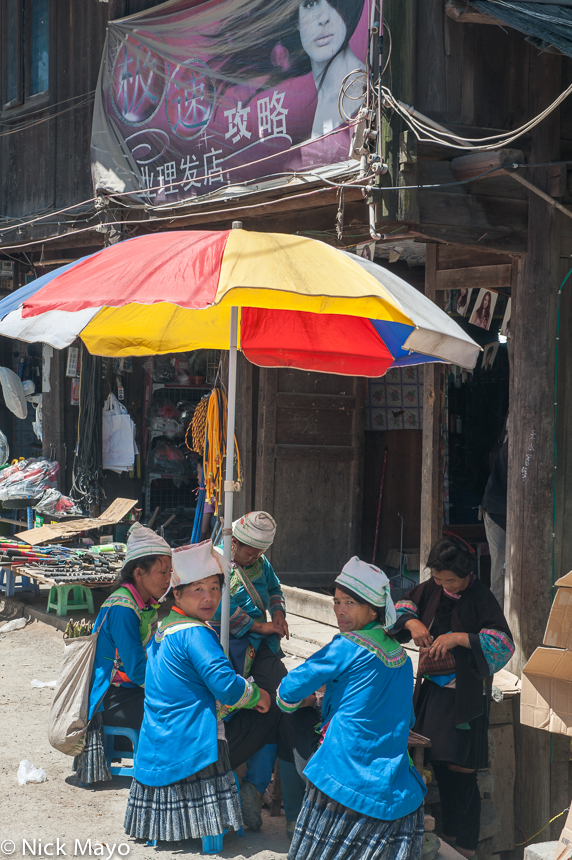 Four Miao women sitting underneath an umbrella on market day in Jia Jou.