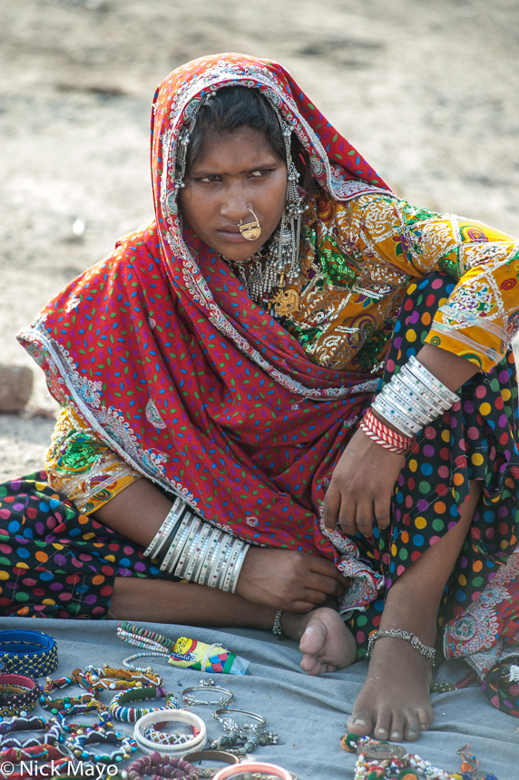 A Mir woman, wearing traditional clothes, head scarf, nose ring, bracelets and anklets, selling jewellery at a small market in...