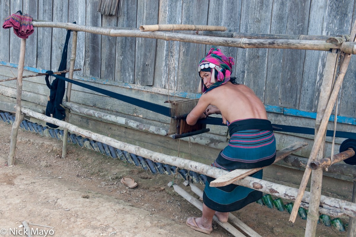 A Ya-er Akha (Hani) woman, wearing a traditional skirt and headdress, weaving on a foot treadle loom in the village of Huey Pot...