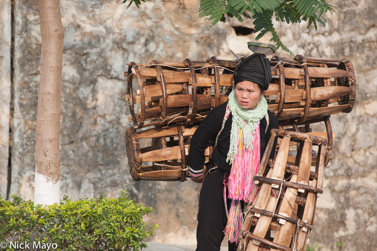 A Yao woman in traditional clothes and hat carrying stools to Nafa market.