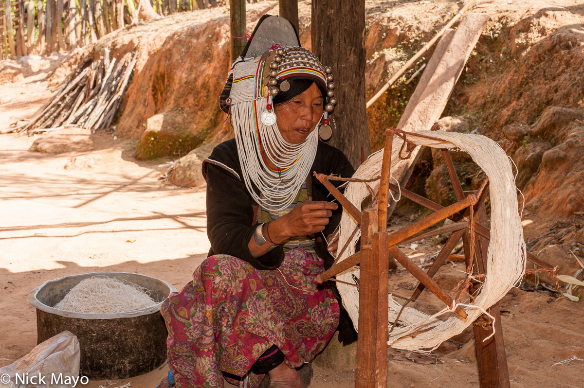 A Loimi Akha (Hani) woman in a traditional headdress spinning thread on a hand powered spindle in the village of Holap I.