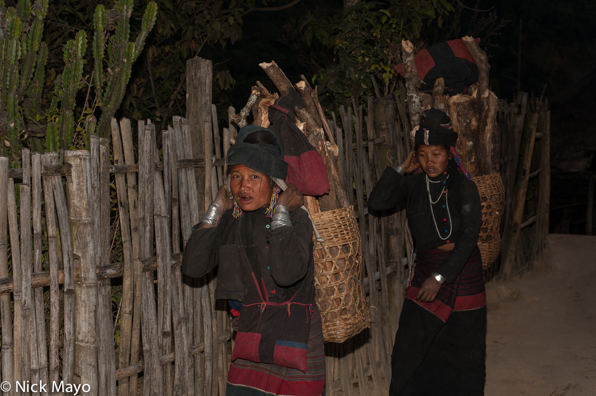 Two Eng women carrying firewood in backstrap baskets to the village of Ban Nong.