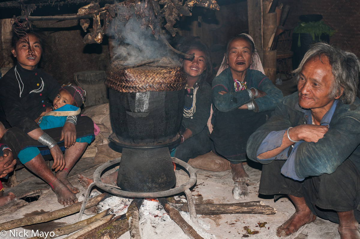 An Eng family seated around the cooking pot on a hearth in their house in Ban Nong.