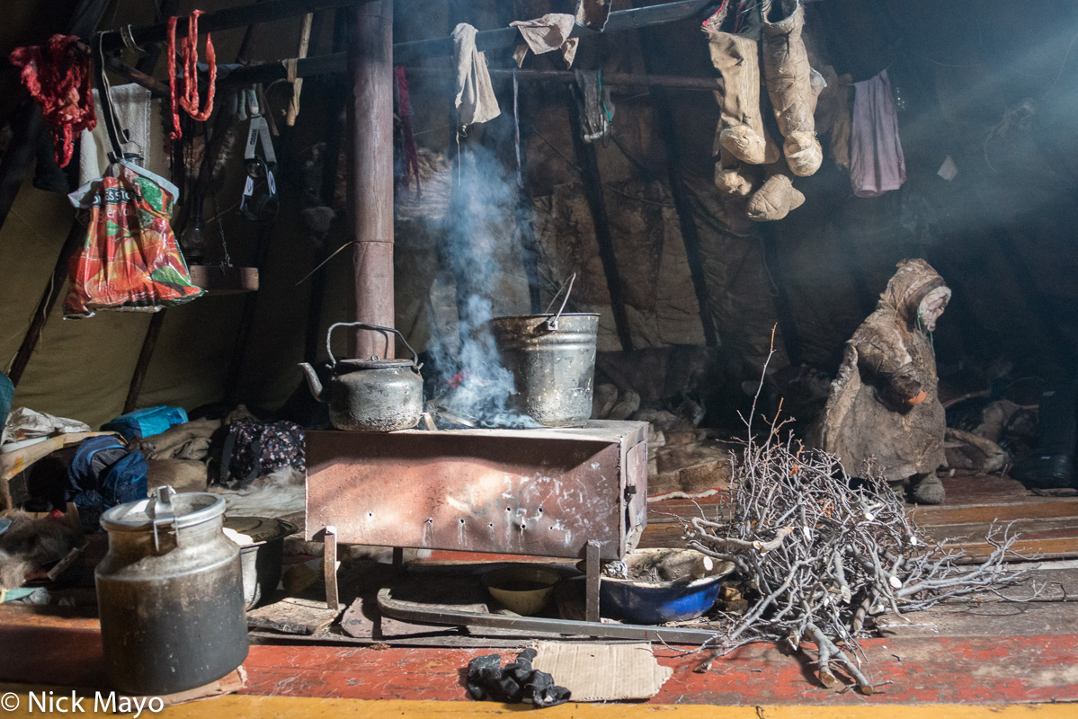 The stove, with its kettle for boiling tea, and a Nenets child wearing a malitsa, inside a chum at a camp on the Yamal peninsula...