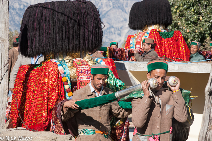 Two Kinnaur men wearing traditional green hats carrying a palanquin at a festival in Kalpa.