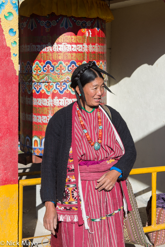 A Monpa woman, wearing a traditional hat and necklace, standing besides a prayer wheel at the Torgya festival in the Tawang monastery...