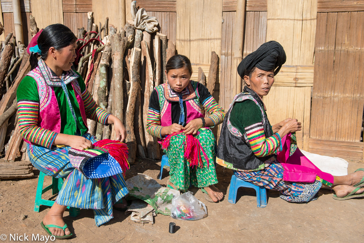 A White Hmong group in their traditional clothes and peaked turbans sewing in the village of Chen Jia Jie.