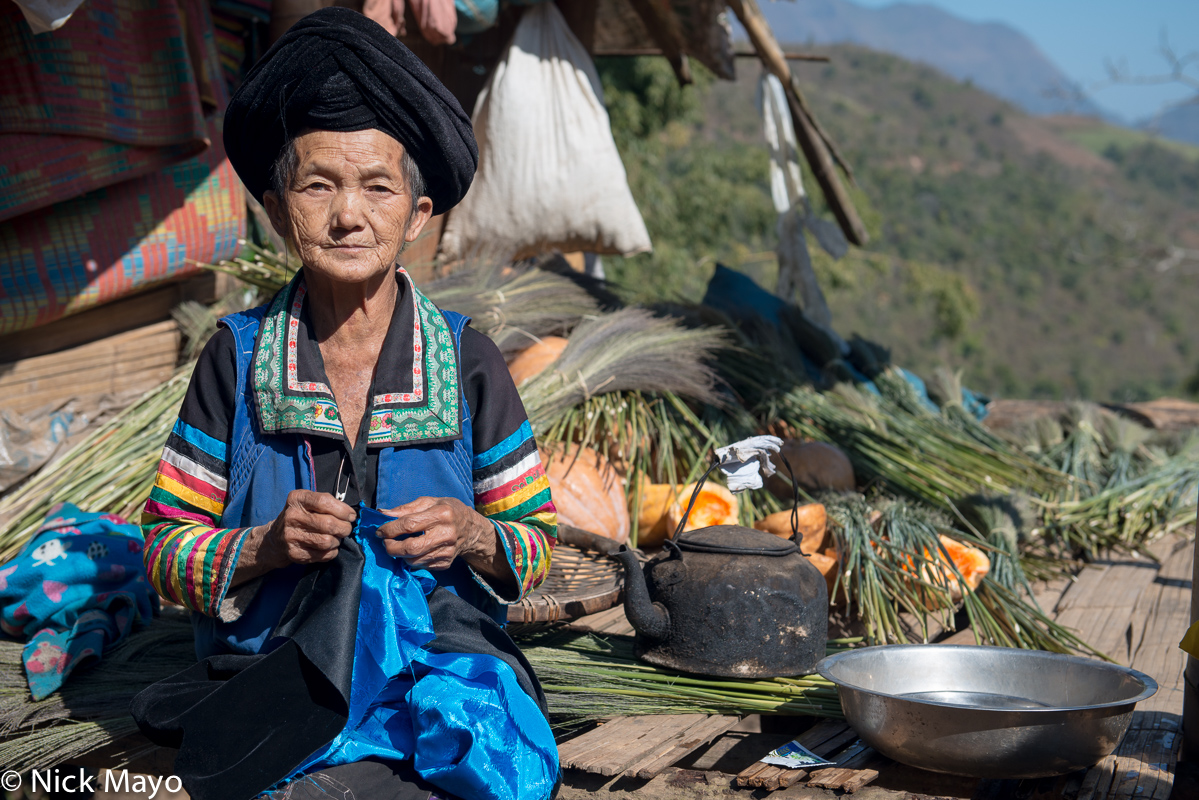 A White Hmong woman in her traditional clothes and peaked turban sewing in the village of Chen Jia Jie.