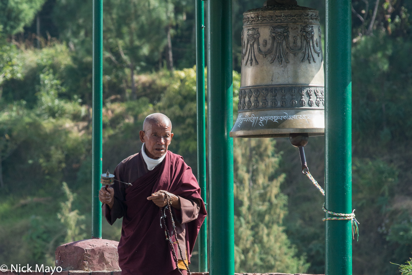 A monk with his prayer wheel and prayer beads by the Rangjung Woesel Choling monastery bell.