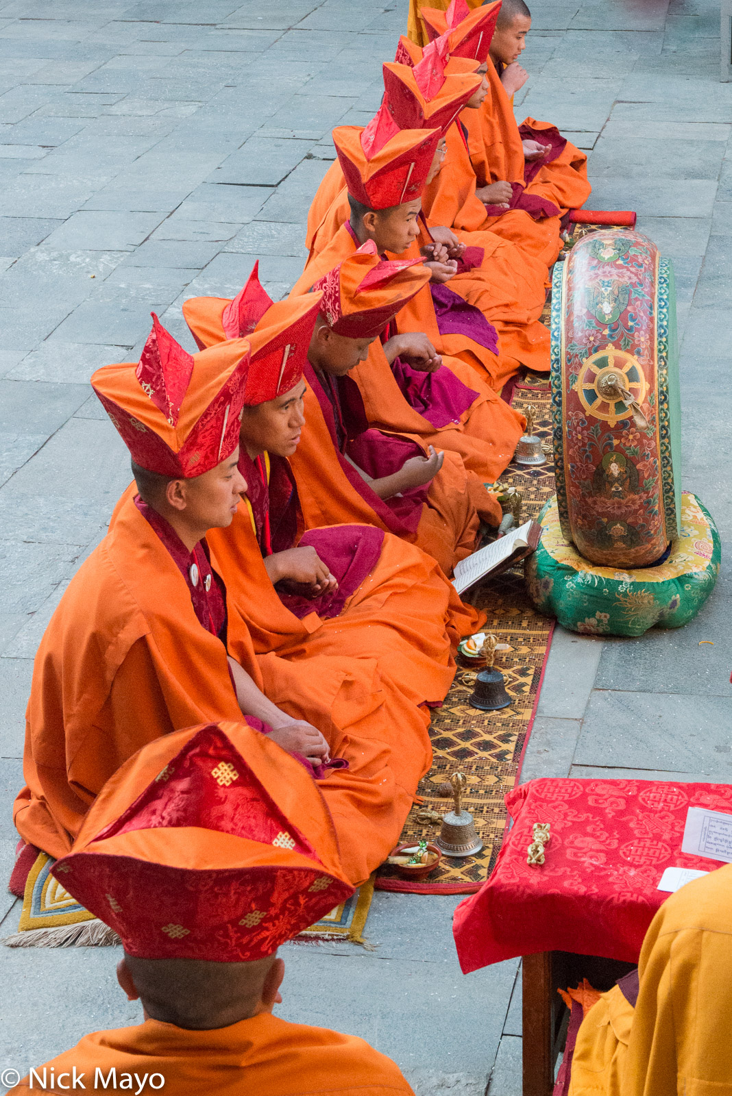 Monks wearing three peaked hats seated in front of a drum at a ceremony during the annual Mongar tshechu.