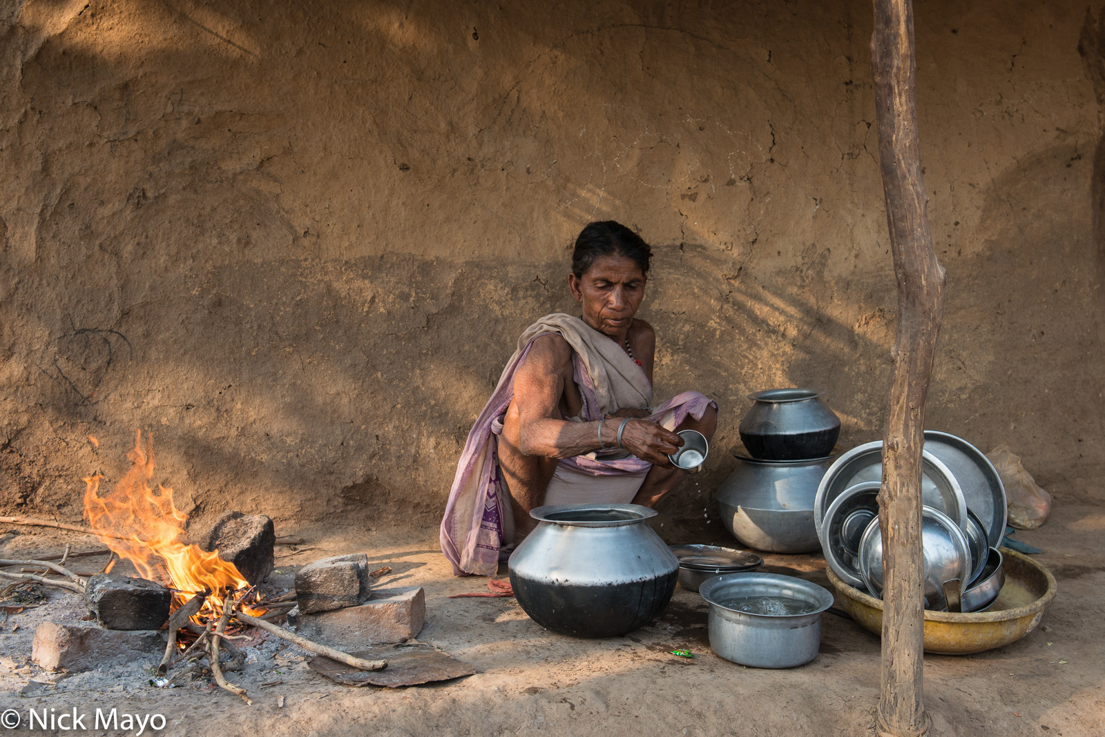 A woman cleaning pots by an open hearth in the Gond village of Bogla.