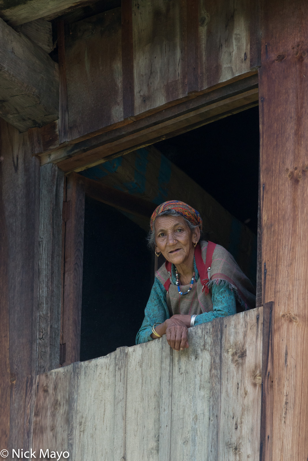 An older woman, wearing traditional bracelets and necklace, at her window in the village of Jana.