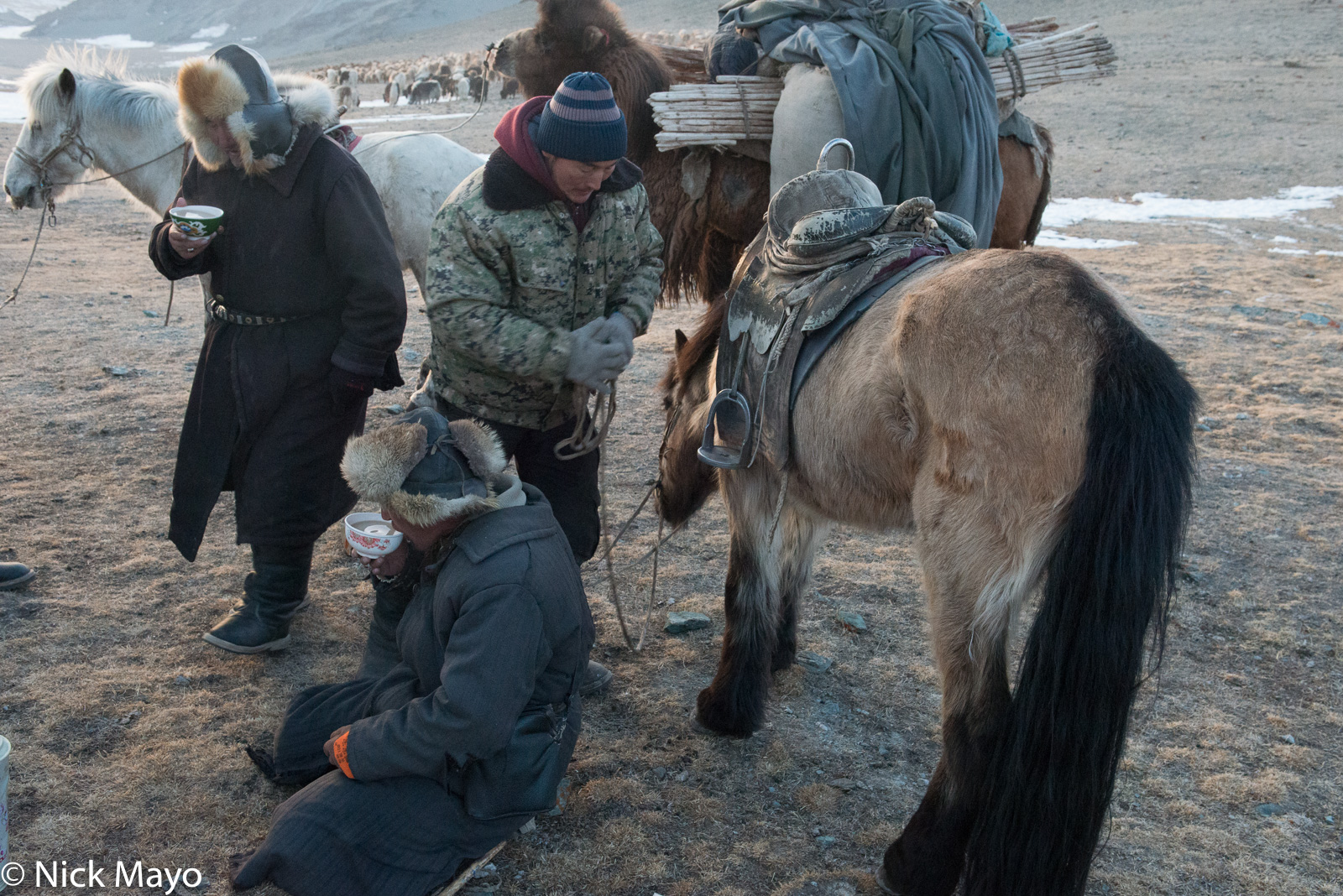 On an intensely cold day in Sagsai sum, Kazakh herders drink tea during a break in the spring migration while their horses and...