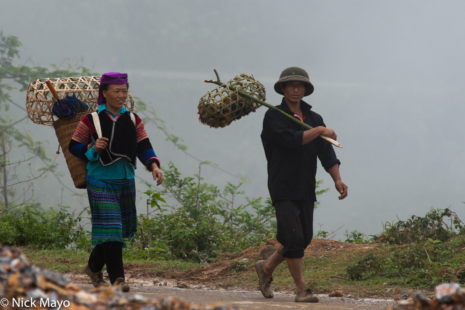 A Hmong couple, her carrying a backstrap basket, him with a bamboo basket on a shoulder pole, walking home from Tua Chua market...