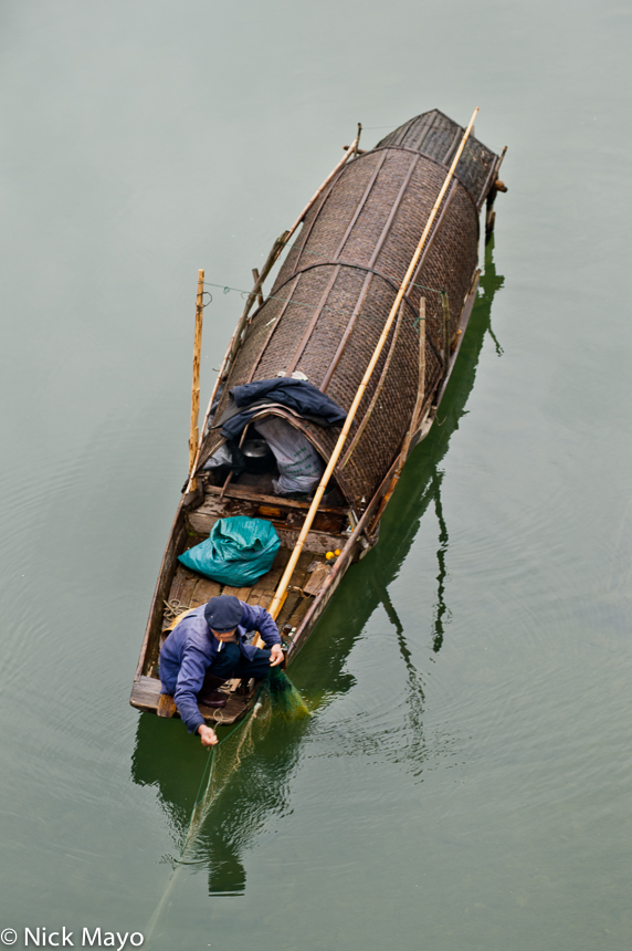 A man pulling in his fishing net from his boat on a river near Yang Dong village.