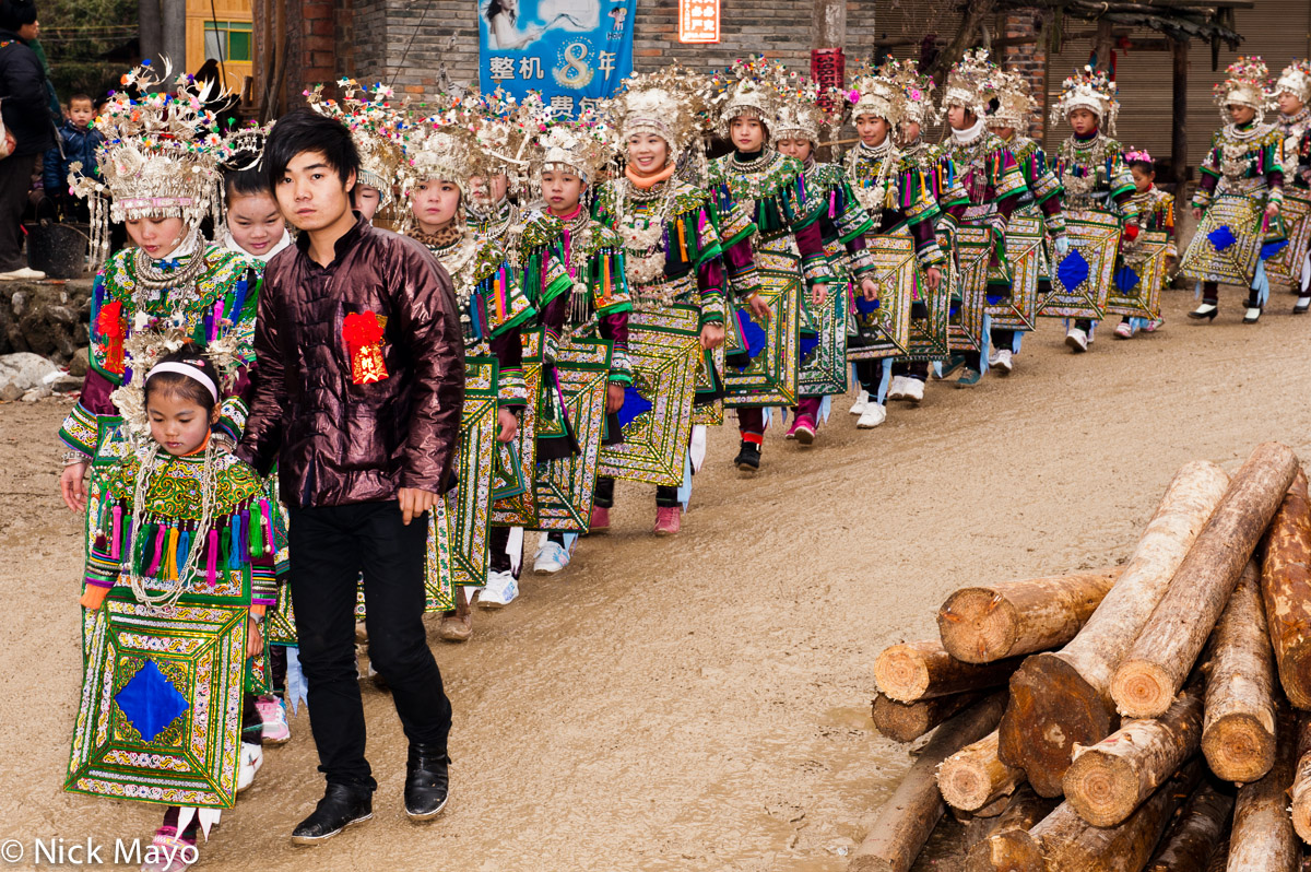 Unmarried girls wearing traditional aprons, headdresses, breastpieces and necklaces in a wedding column in the village of Yang...