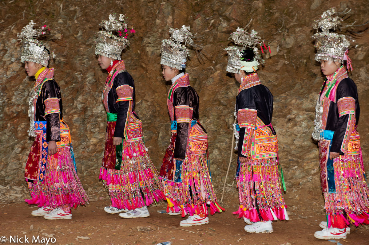 Miao girls in full festival attire, including crown headdresses and breastpieces, circling in the bullfight arena near Jiuli...
