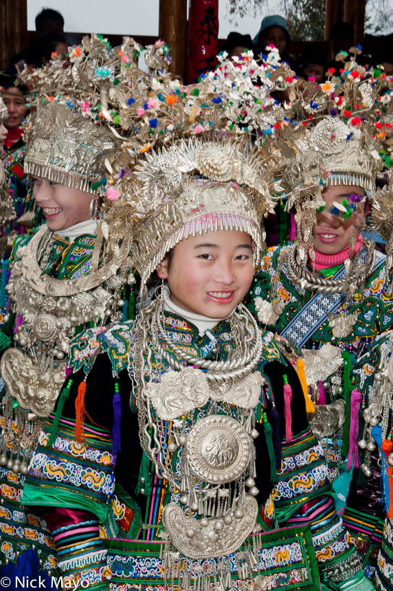 Miao girls in full festival attire, including crown headdresses, breastpieces, earrings and necklaces, at a village festival...